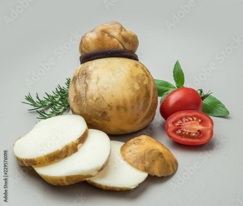 Traditional Italian Scamorza  cheese with tomato and herbs on gray background.