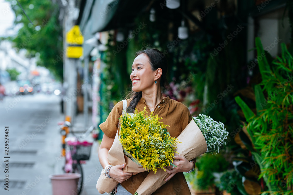 © LUMINA IMAGES - Beautiful Asian woman enjoying shopping outdoors and holding flowers. © LUMINA IMAGES - Beautiful Asian woman enjoying shopping outdoors and holding flowers.
