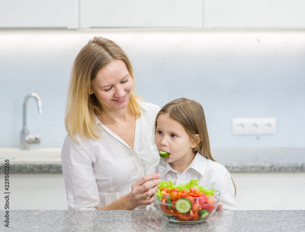 mother and daughter eating vegetables at kitchen