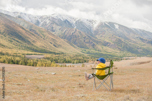 Little girl in the tourist chair enjoys the view of the peaks of the snow mountains. Empty space for text