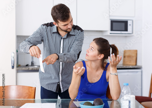 Upset young man with bill having conflict with girl in home interior