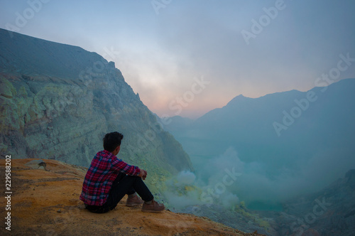 Young man sitting on top of mountain and looking view of sunrise over the lake.