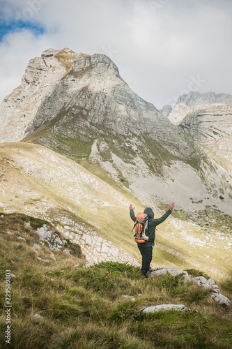 Hiking man with backpacker open arms looking mountain peaks