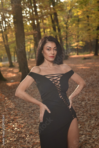Beautiful woman wearing a long black dress posing in the woods on a sunny autumn afternoon.