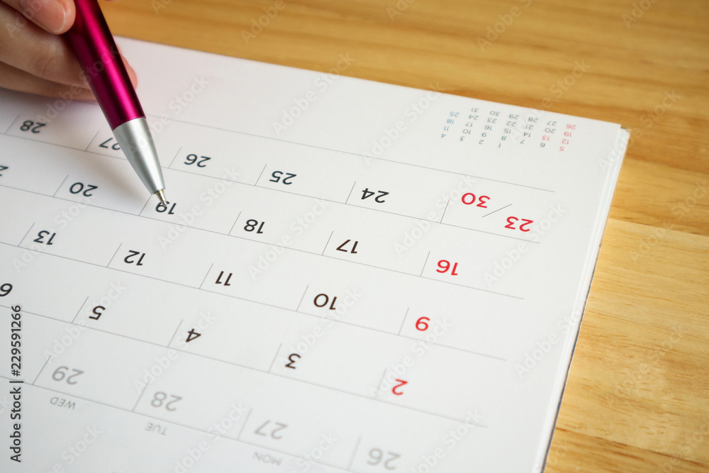 calendar page with female hand holding pen on desk table calendar page with female hand holding pen on desk table