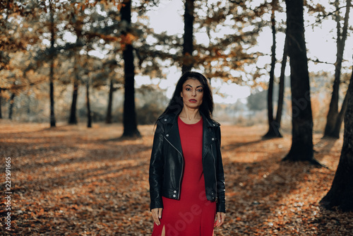 Young woman wearing a long red dress posing on a an autumn day in the woods.