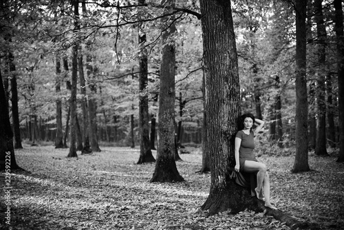 Young woman wearing a long red dress posing on a an autumn day in the woods.