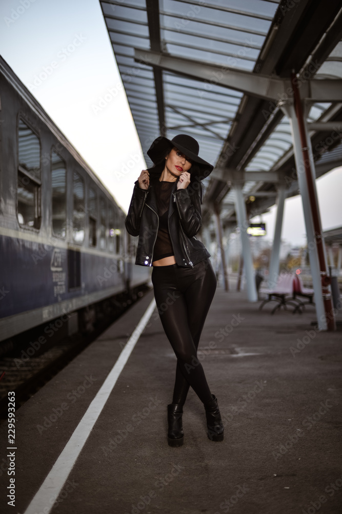 Obraz premium Young sexy woman dressed in black posing on a train station pier.