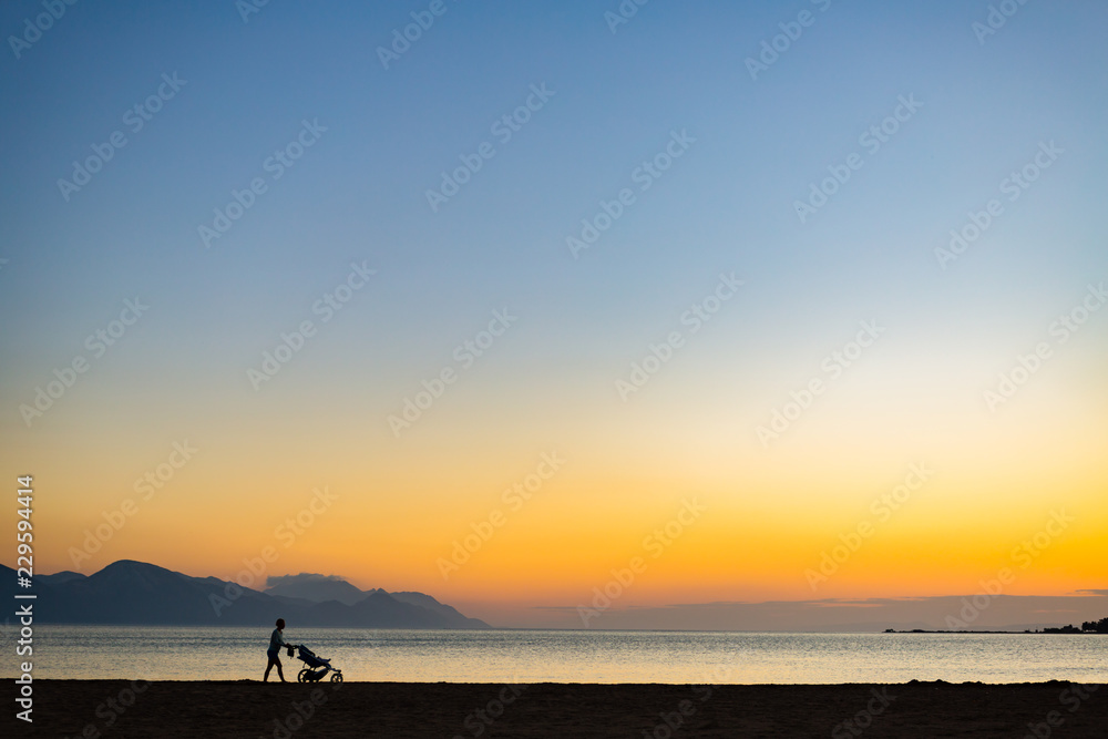 Silhouette of mother with baby stroller enjoying motherhood at sunset landscape