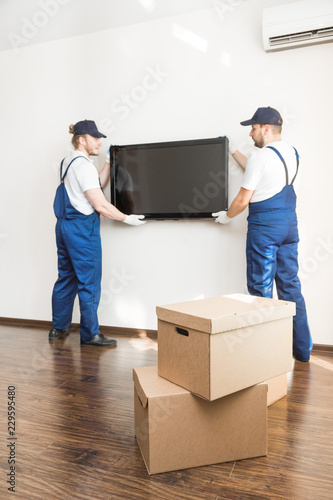 Delivery manremove the TV from the wall for moving to an apartment. professional worker of transportation, male loaders in overalls