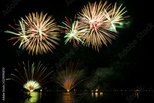 Colorful fireworks explosions in the night reflecting in water © Simon
