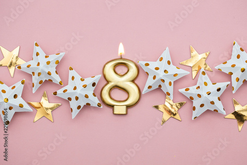 Photography Number 8 gold candle and stars on a pastel pink background