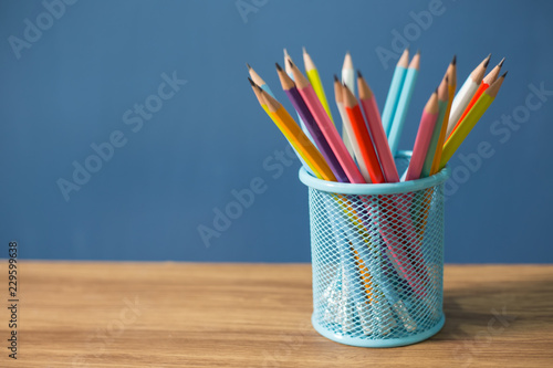 Colorful pencils in metal holder on blue background