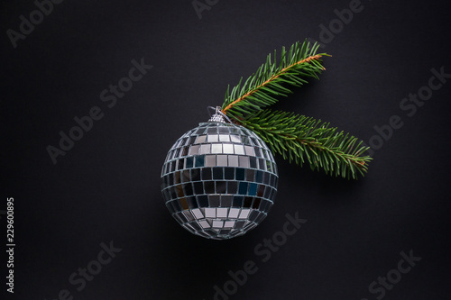 Big bauble made of mirror pieces decorated with spruce twigs against black background