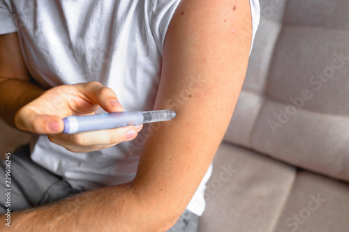 close up of handsome stylish young teen caucasian with syringe inject insulin to his shoulder himself at home .  Diabetes patient shot by syringe with dose, subcutaneous hand vaccination concept 