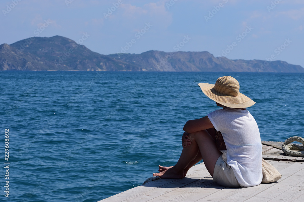 Young woman with sun hat relaxing on the quay of Port Sostis, Zakynthos Island, Greece