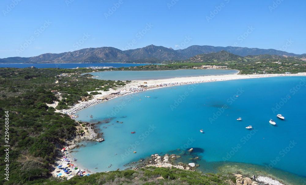 View from above over the white beach, tranquil bay, distant mountains and blue water of the Mediterranean Sea at Porto Giunco, Sardinia, Italy