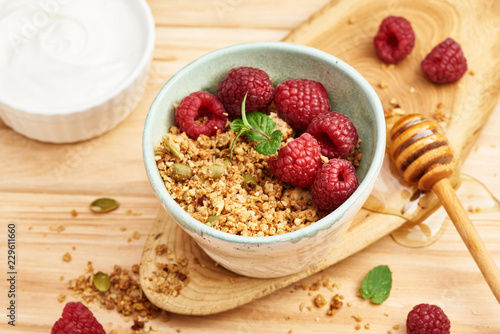 Homemade granola and yogurt in a bowl with raspberries on a wooden table.