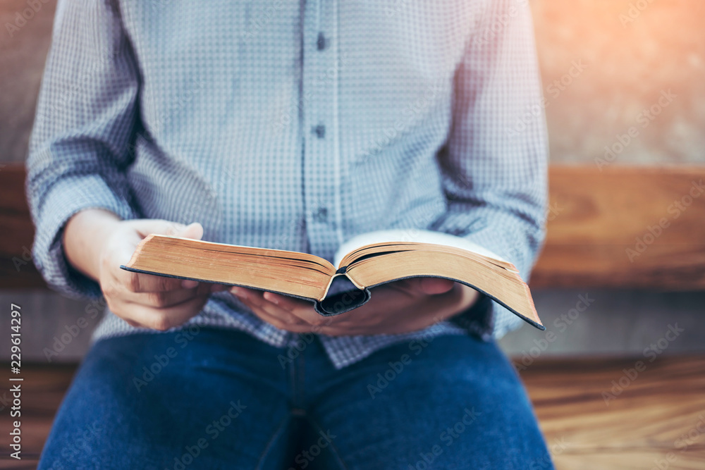 Fototapeta premium a man sit on wooden chair and reading bible or book over concrete wall with window light