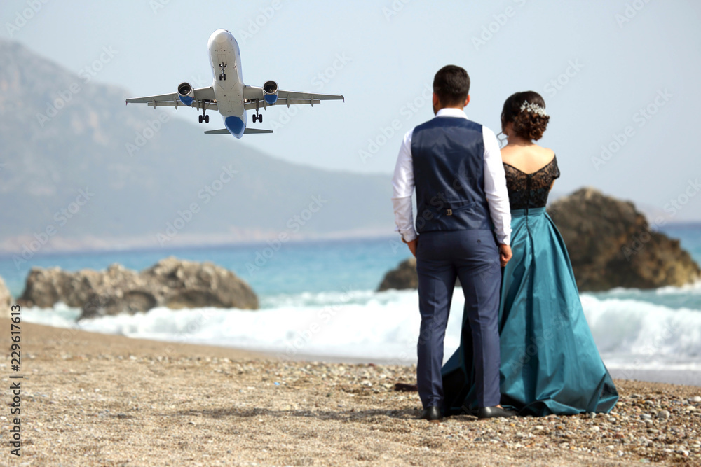 man and a woman looking at a passenger plane flying by the sea