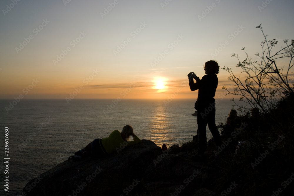 Eine Frau fotografiert den Sonnenuntergang am Meer / Woman photographs the sunset by the sea