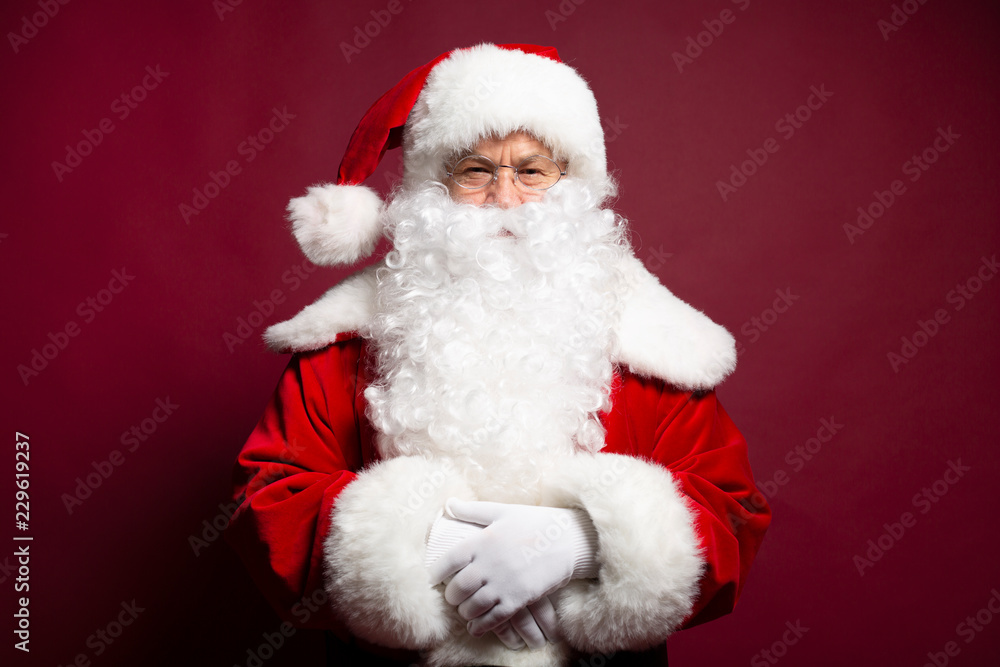Portrait of man in Santa Clause costume looking at camera while posing on red background, Christmas and New year concept Portrait of man in Santa Clause costume looking at camera while posing on red background, Christmas and New year concept
