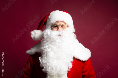 Portrait of man in Santa Clause costume looking at camera while posing on red background, Christmas and New year concept