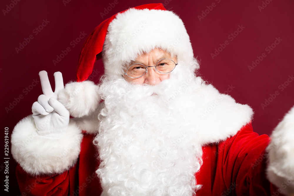 Portrait Santa Clause showing peace sign and makes selfie photo on red background, Christmas and New year concept Portrait Santa Clause showing peace sign and makes selfie photo on red background, Christmas and New year concept