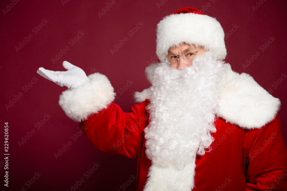 Portrait of man in Santa Clause costume pointing with hand aside on red background, Christmas and New year concept