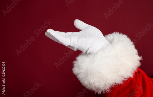Male hand in white glove and Santa Clause costume on red background, Christmas and New year concept