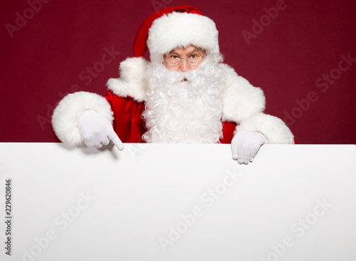 Santa Clause pointing at white blank banner on red background, Christmas and New year concept