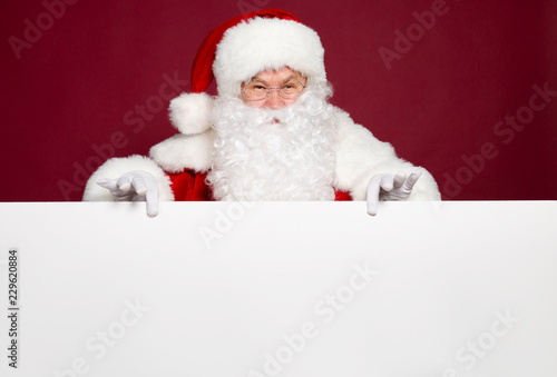 Happy grandfather in Santa Clause costume holding big white blank banner on red background, Christmas and New year concept © My Ocean studio