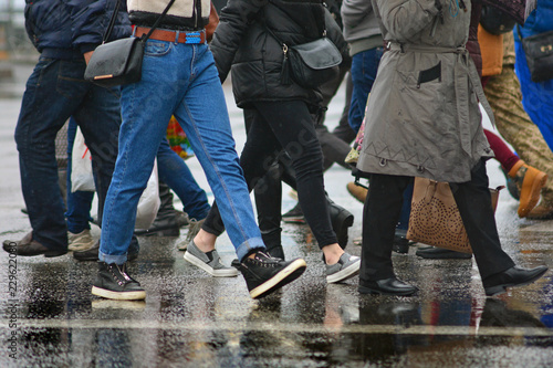 People crowd on a pedestrian crosswalk. Wet weather in city.