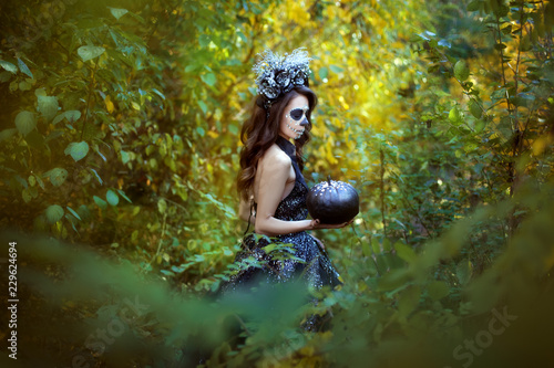 Fototapeta Naklejka Na Ścianę i Meble -  Young woman in costume for Halloween stands with a pumpkin in the forest.