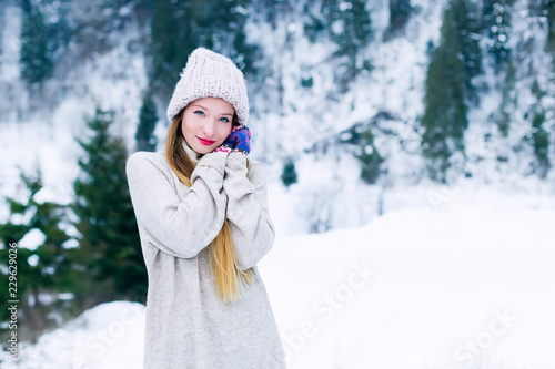 girl in warm clothes look at camera and hold her hands near her face against the background of snow-capped mountains