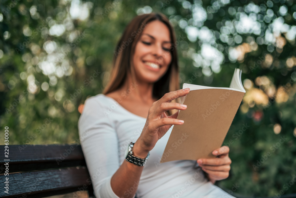 Fototapeta premium Enjoying a book outdoors. Girl reading a book on a bench in the park. Focus on the book.