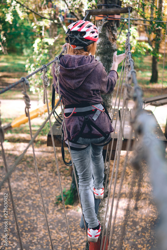 happy girl, women, climbing gear in an adventure park are engaged in rock climbing on the rope road, arboretum, insurance, attraction, amusement park, active recreation, autmn, vertical photo