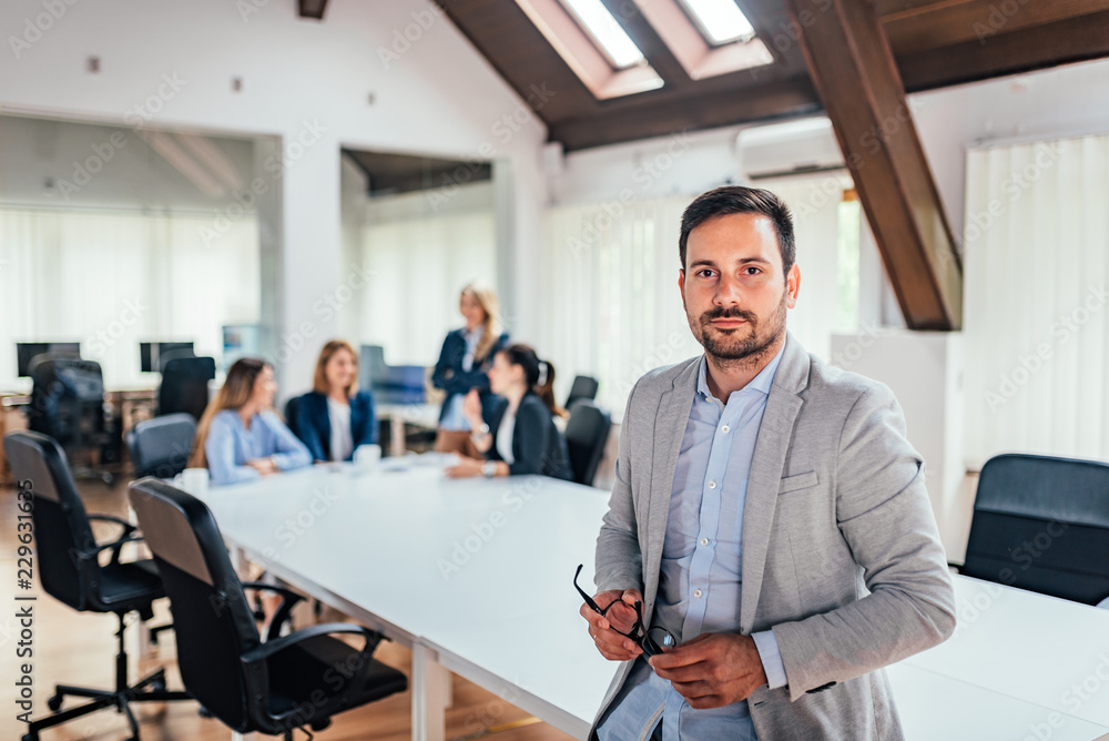 Portrait of successful businessman with people in background at office meeting. Portrait of successful businessman with people in background at office meeting.