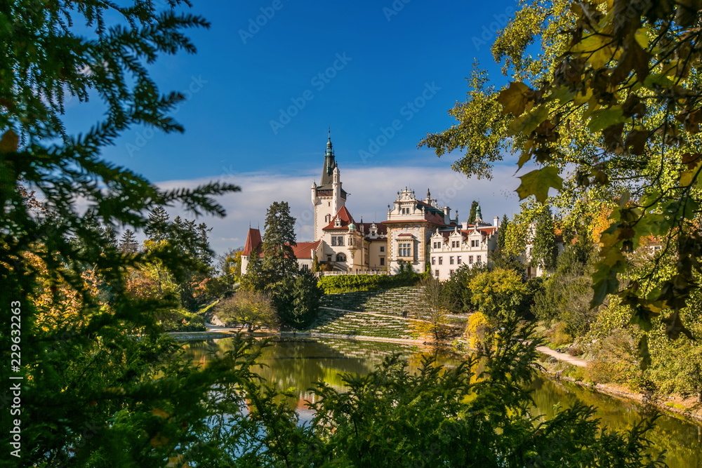 Scenic landscape of famous romantic Pruhonice castle, Czech Republic, Europe, standing on hill in a park, sunny colorful fall day, blue sky, spruce branches and maple leaves framing picture