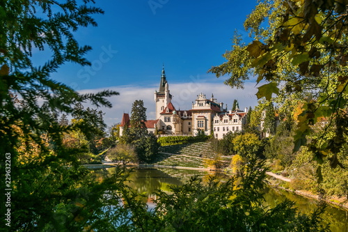 Scenic landscape of famous romantic Pruhonice castle, Czech Republic, Europe, standing on hill in a park, sunny colorful fall day, blue sky, spruce branches and maple leaves framing picture