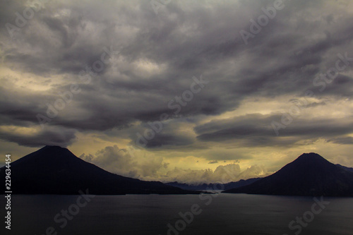Stunning landscape view across Lake Atitlan (Lago de Atitlán) to the volcanoes Volcán Tolimán, Volcán Atitlán, and Volcán San Pedro, in Guatemala, Central America, with dramatic clouds.