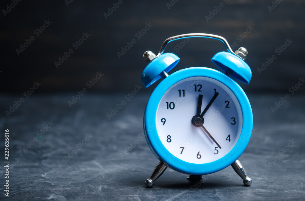 The blue alarm clock indicates the beginning of the first on a black background. time management. concept of the flow of time. copy space. minimalist style. The blue alarm clock indicates the beginning of the first on a black background. time management. concept of the flow of time. copy space. minimalist style.