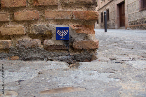 A blue pottery tile with a yellow menorah on it in a brick wall in the Jewish quarter of Toledo, Castile-La Mancha, Spain, a UNESCO World Heritage Site