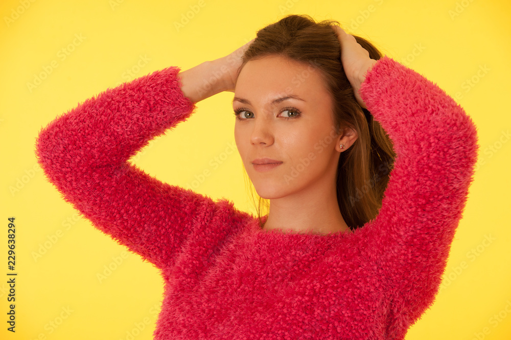 Portrait of a beautiful young woman in pink sweater over yellow background Portrait of a beautiful young woman in pink sweater over yellow background