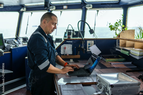 Marine navigational officer or technician is using laptop or notebook at sea. Job at sea