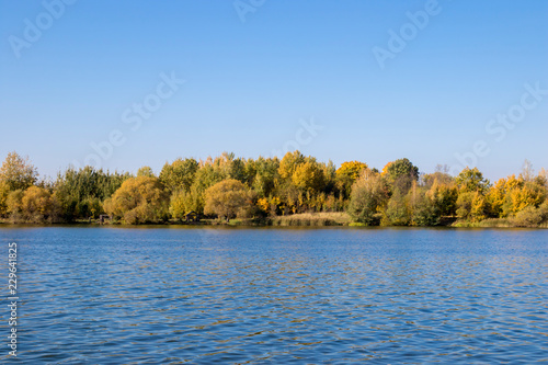 Lake and golden trees on blue sky background