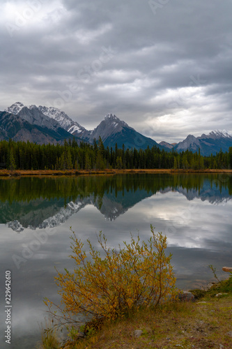 The foothills of the Rockies reflecting in an alpine lake as a moody storm roles in © Jesse