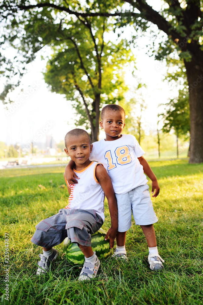 two happy black African American baby boy sitting on a big watermelon smiling on a Park background on a summer day.