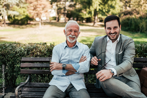 Portrait of a business family outdoors. Two men sitting in the park looking at camera. photo
