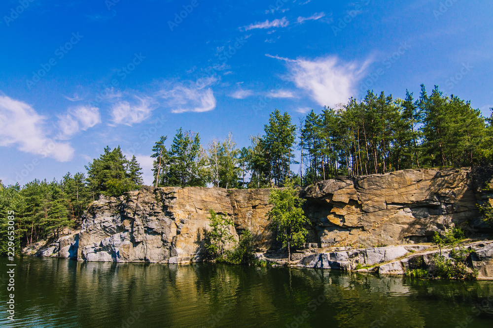 Korostyshiv Canyon, deep lake in Zhytomir region with green water and blue sky in Ukraine and fir forest around Korostyshiv Canyon, deep lake in Zhytomir region with green water and blue sky in Ukraine and fir forest around